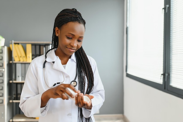 Nahaufnahme einer abgeschnittenen horizontalen Aufnahme einer lächelnden afrikanischen Ärztin oder Apothekerin, die bunte Blasen mit Pillen hält, die sie der Kamera zeigen, während sie in der Apotheke oder im Krankenhaus stehen