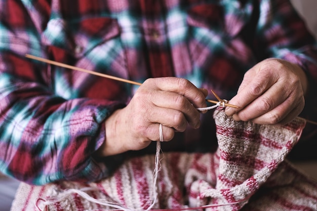 Nahaufnahme einer älteren Frau, die mit den Händen einen Pullover mit Nadeln strickt, um die Familie und die Liebe des Enkelkindes zu stärken