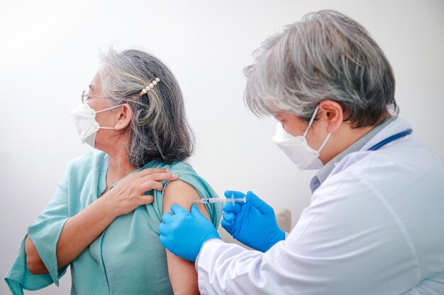 Nahaufnahme einer älteren frau, die von einem männlichen arzt mit blauen handschuhen eine coronavirus-impfung erhält, um das immunsystem zu stärken, um eine infektion zu verhindern. impfung für ältere menschen