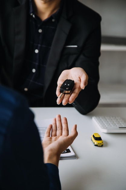 Nahaufnahme einer asiatischen Frau, die ein Autoversicherungsdokument oder einen Mietvertrag oder eine Vereinbarung unterzeichnet Kauf oder Verkauf von neuen oder gebrauchten Fahrzeugen mit Autoschlüsseln auf dem Tisch