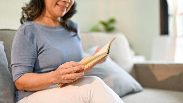 Nahaufnahme einer asiatischen Frau, die ein Buch auf dem Sofa in ihrem Wohnzimmer liest