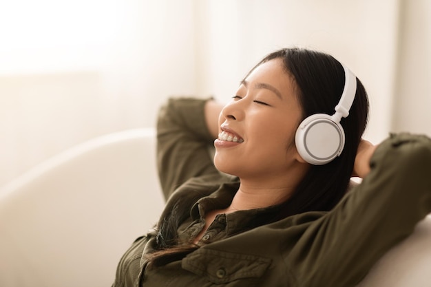 Nahaufnahme einer asiatischen Frau, die zu Hause drahtlose Kopfhörer verwendet