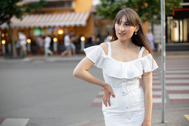 Nahaufnahme einer attraktiven brünetten Frau in einem weißen Kleid, die vor dem Hintergrund der Straße und der grünen Bäume zur Seite schaut. der Platz für dein Design