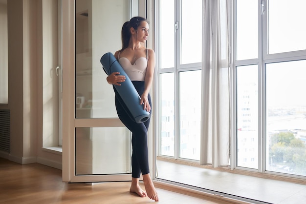 Nahaufnahme einer attraktiven jungen Frau, die vor dem Training im Studio eine blaue Yoga- oder Fitnessmatte auslegt Gesunder Lebensstil