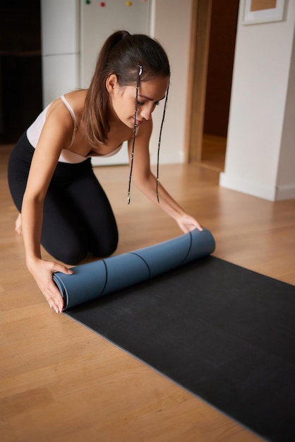 Nahaufnahme einer attraktiven jungen Frau, die vor dem Training im Studio eine blaue Yoga- oder Fitnessmatte auslegt Gesunder Lebensstil
