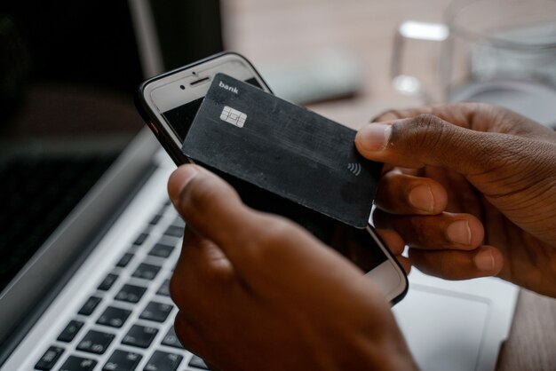 Nahaufnahme einer Bank-Plastikkarte. Schwarze Kreditkarte oder Einzahlung in Händen vor dem Hintergrund eines Arbeitsplatzes mit Laptop und Smartphone.