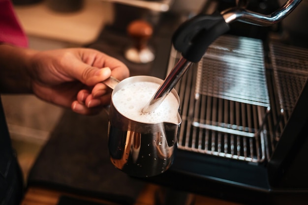Nahaufnahme einer Barista-Hand, die einen Hochdruck-Dampfschäumer verwendet, um einen Cappuccino-Kaffee zuzubereiten