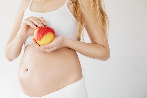 Nahaufnahme einer blonden schwangeren Frau, die einen natürlichen Apfel voller Vitamine und Eisen hält Konzept der vorgeburtlichen Ernährung Kopieren Sie Platz High Key