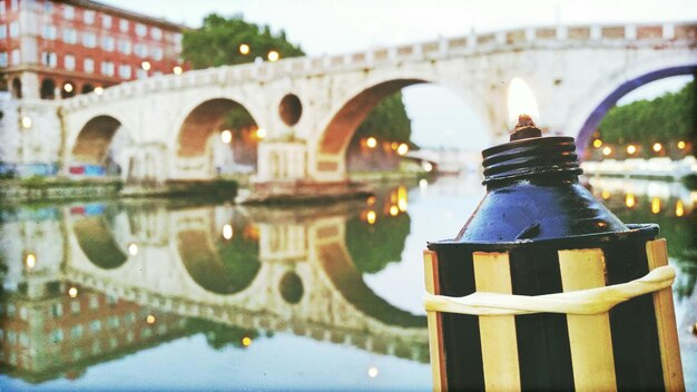 Foto nahaufnahme einer brennenden tiki-fackel am fluss gegen die brücke