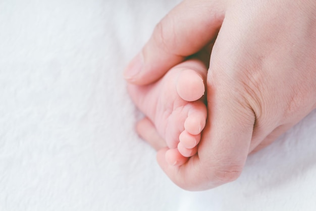 Nahaufnahme einer Elternhand, die den Fuß des Babys zu Hause auf dem Bett hält