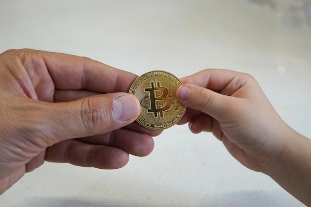 Nahaufnahme einer erwachsenen Hand, die einem Kind auf weißem Hintergrund eine Bitcoin gibt