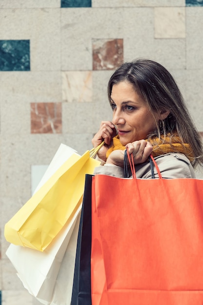 Nahaufnahme einer erwachsenen lächelnden Frau, die bunte Taschen des Einkaufs hält.