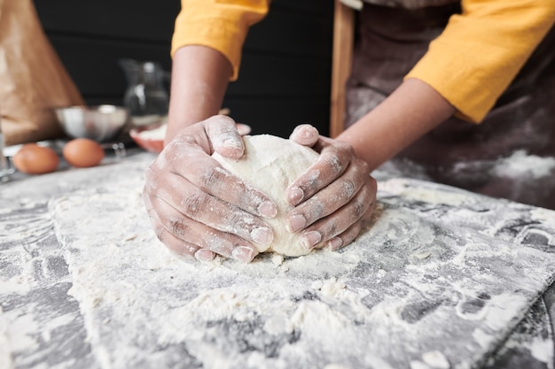 Nahaufnahme einer Frau, die am Tisch einen Teig für Kuchen knetet