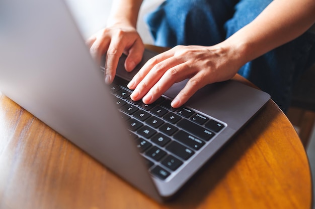 Nahaufnahme einer Frau, die auf der Tastatur eines Laptops auf dem Tisch arbeitet und tippt