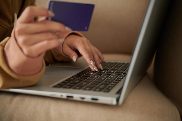 Nahaufnahme einer Frau, die auf der Tastatur eines Laptops tippt, während sie auf dem Sofa liegt und die Kartennummer eingibt, um Rechnungen zu bezahlen