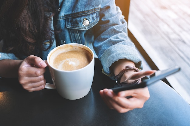 Nahaufnahme einer Frau, die beim Kaffeetrinken ein Handy hält und benutzt