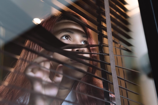 Foto nahaufnahme einer frau, die durch jalousien und fenster wegblickt