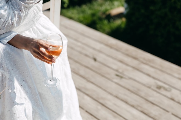 Nahaufnahme einer Frau, die ein weißes Sommerkleid trägt und ein Glas Champagner hält