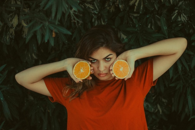 Nahaufnahme einer Frau, die eine Orange gegen einen Baum hält