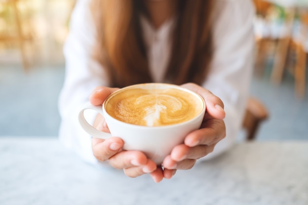 Nahaufnahme einer Frau, die eine Tasse heißen Kaffee hält und zeigt