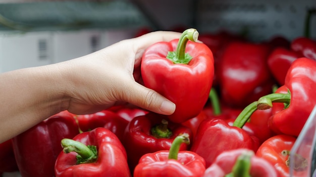 Nahaufnahme einer Frau, die frische rote Paprika auf dem Regal im Supermarkt hält