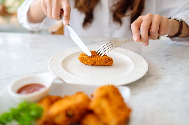 Nahaufnahme einer Frau, die Messer und Gabel benutzt, um Brathähnchen im Restaurant zu essen?