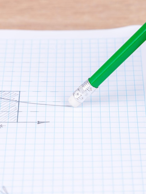 Nahaufnahme einer Frau, die mit einem Gummiband auf einem Schieferbleistift in einem karierten Notizbuch eine Grafik radiert