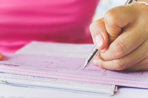 Nahaufnahme einer Frau, die mit einem Stift auf Papier schreibt