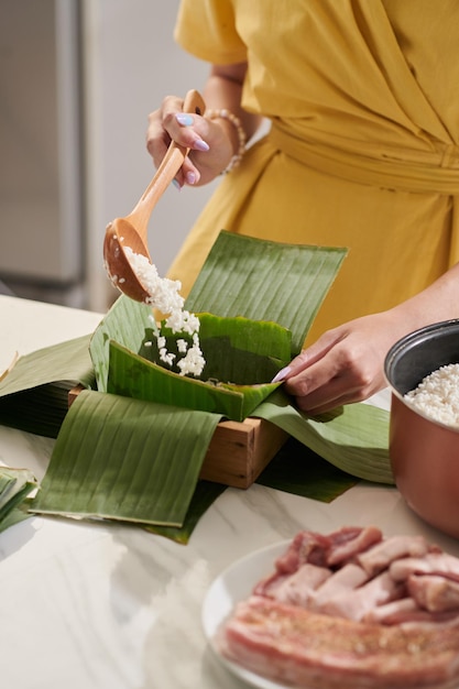 Nahaufnahme einer Frau, die Reis auf Bananenblätter legt, wenn sie für Tet kocht