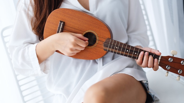 Nahaufnahme einer Frau, die sitzt und Ukulele im Schlafzimmer spielt