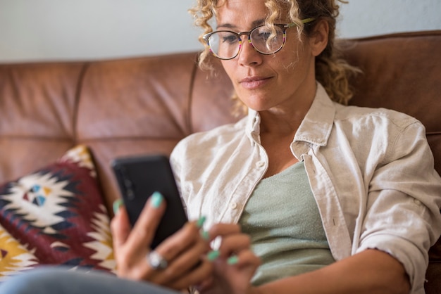 Nahaufnahme einer Frau, die zu Hause ein modernes Smartphone verwendet, das auf dem Sofa sitzt und die drahtlose Internetverbindung genießt, weibliche Menschen mit Anwendung auf Mobiltelefonschreiben oder E-Mail-Benachrichtigungen lesen