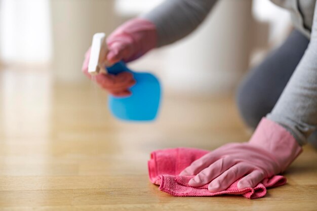 Nahaufnahme einer Frau, die zu Hause Reinigungsmittel sprüht und Parkett reinigt