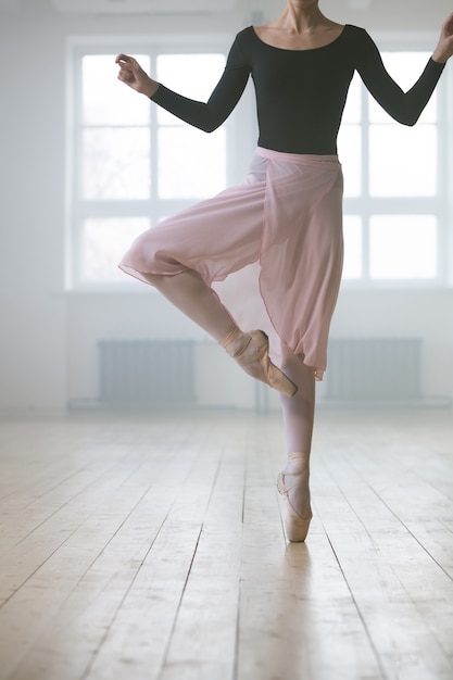 Nahaufnahme einer Frau im Tutu-Kleid und in Spitzenschuhen, die auf einem Bein steht und im Studio Ballett übt