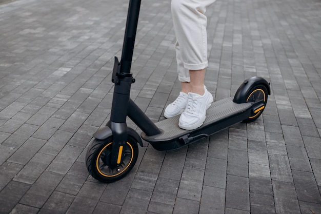 Nahaufnahme einer Frau im weißen Anzug, die auf ihrem Elektroroller in der Stadt steht