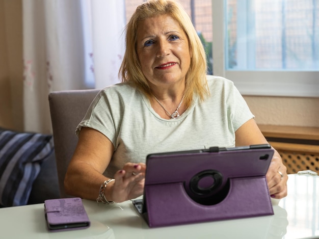 Nahaufnahme einer Frau in ihren 60ern, die zu Hause mit ihrem Tablet sitzt und glücklich ist