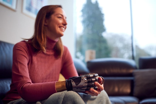 Nahaufnahme einer Frau mit Arm- und Handprothese, die sich zu Hause auf dem Sofa entspannt und eine Tasse Kaffee trinkt