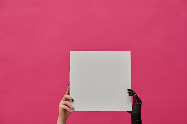 Nahaufnahme einer Frau mit einer gesunden Hand und einer prothetischen Hand, die ein Plakat auf rosa Hintergrund hält