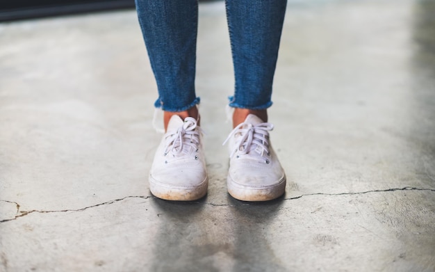 Nahaufnahme einer Frau mit Jeans und weißen Turnschuhen, die auf Betonboden steht