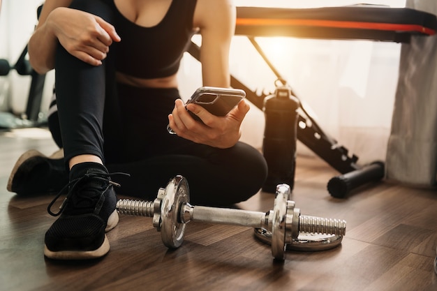 Nahaufnahme einer Frau mit Smartphone beim Training im Fitnessstudio. Sport- und Technologiekonzept. Lifestyle und Gesundheitswesen Thema. Im Morgenlicht