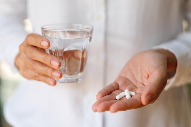 Nahaufnahme einer Frau mit weißen Pillen und einem Glas Wasser