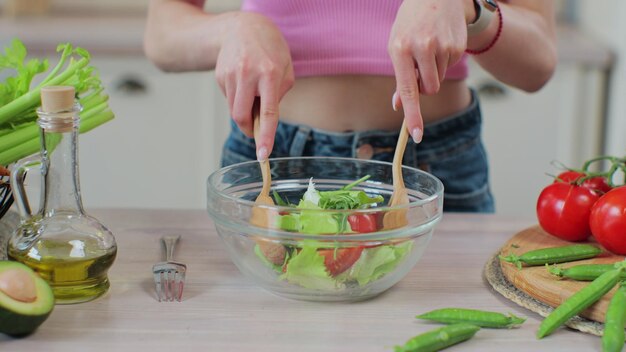 Nahaufnahme einer Frau rührt mit Holzlöffeln frischen Gemüsesalat um. Zubereitung von frischem Gemüsesalat. Gesundes Ernährungs- und Kochkonzept