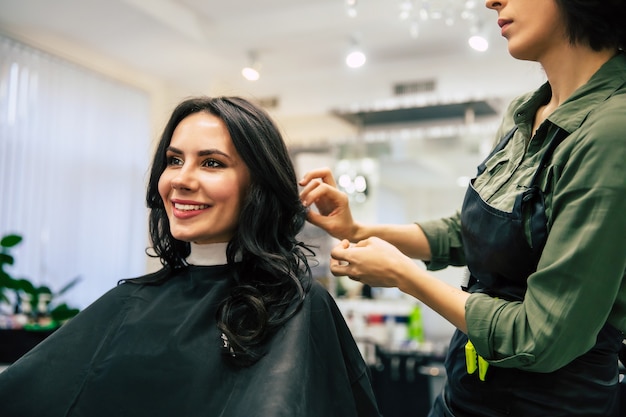 Nahaufnahme einer Friseurin, die das Haar ihres glücklichen Kunden berührt, während sie eine neue Frisur macht.