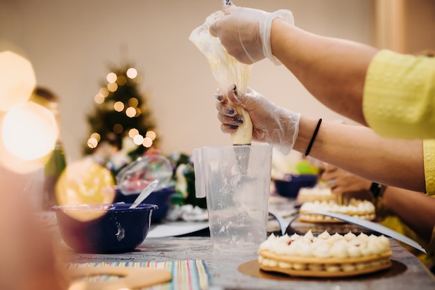 Nahaufnahme einer Gebäckhand, die einen Weihnachtslebkuchen mit einem Spritzbeutel, Arbeitsatmosphäre verziert. Ansicht über der Schulter.