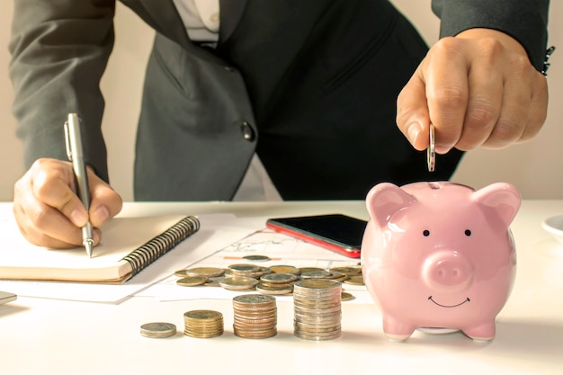 Nahaufnahme einer Geschäftsfrau, die eine Münze in einem Sparschwein hält, ein Konzept des Geldsparens für die Finanzbuchhaltung.