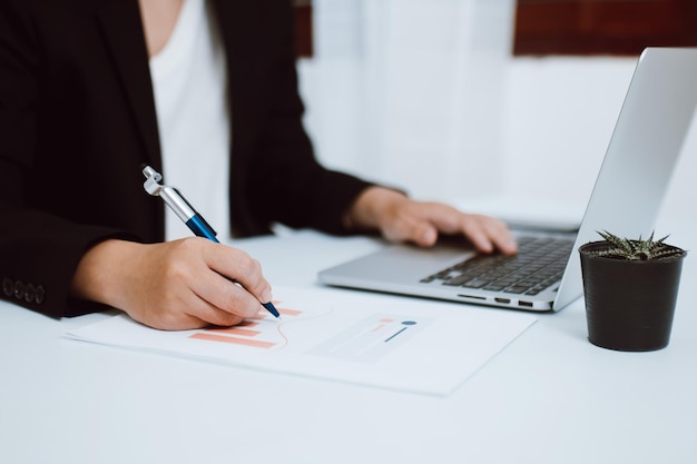 Nahaufnahme einer Geschäftsfrau oder eines Buchhalters, die mit einem Dokument und einem Laptop auf dem Tisch arbeiten Buchhaltungsfinanzgeschäftsbericht zur Analyse und Planung von Investitionsfinanzdaten