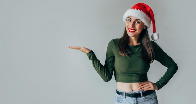 Nahaufnahme einer glücklichen, aufgeregten jungen brünetten Frau mit Weihnachtsmann-Hut, isoliert vor grauem Hintergrund