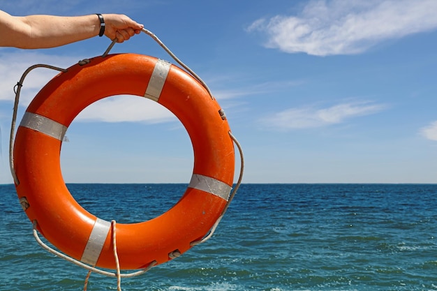 Nahaufnahme einer Hand, die den Rettungsgürtel über dem Meer gegen den Himmel hält