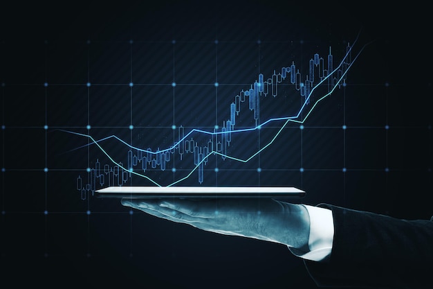 Nahaufnahme einer Hand, die ein Tablet mit leuchtendem Candlestick-Forex-Diagramm auf dunklem Hintergrund hält Handelsfinanzierung und Aktienkonzept