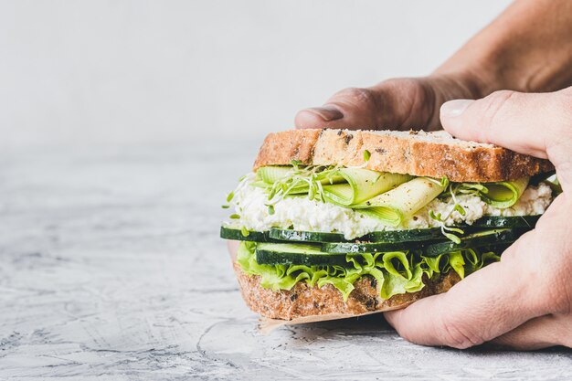 Nahaufnahme einer Hand, die ein vegetarisches Sandwich mit grünem Gemüse hält. Salat, Zucchini, Luzerne und Gurke. Veganes Essen