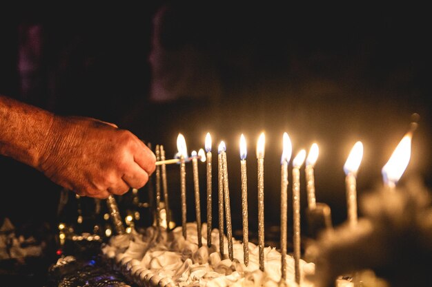 Foto nahaufnahme einer hand, die eine kerze auf einem kuchen im dunkelraum entzündet